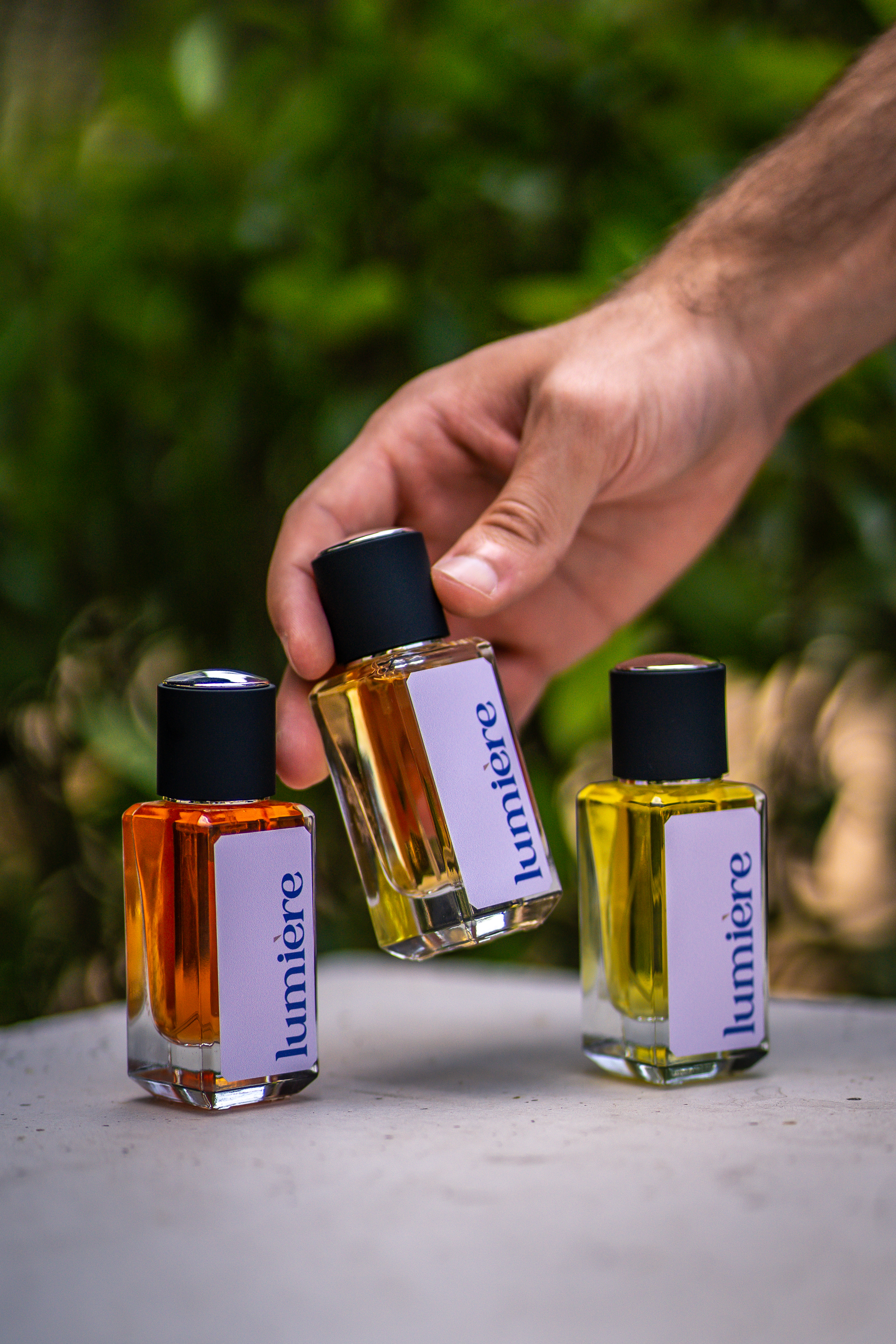 Hand arranging colorful Lumiere perfume bottles on a reflective surface